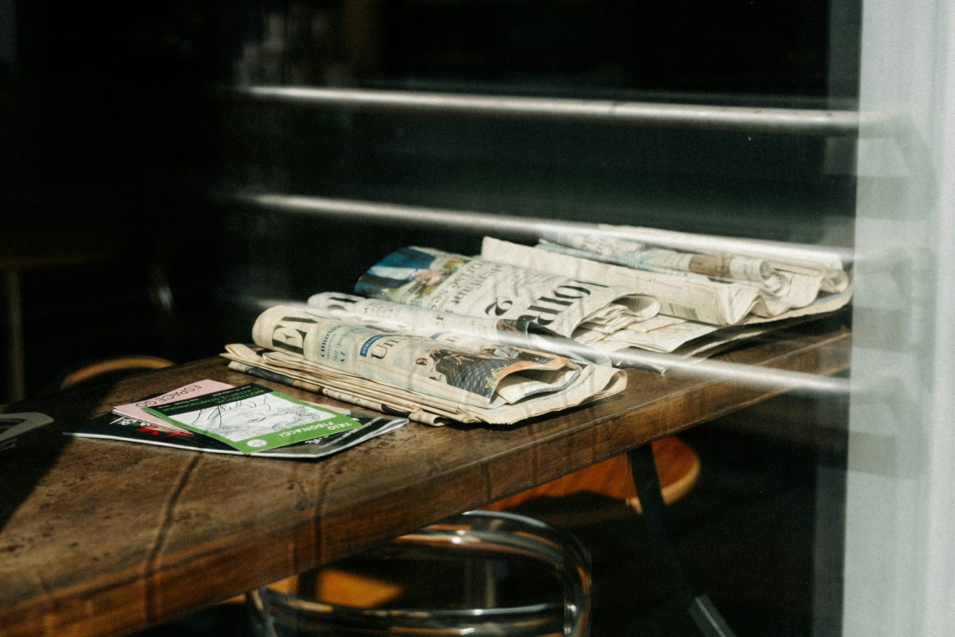 Stack of newspapers and magazines on a wooden table.
